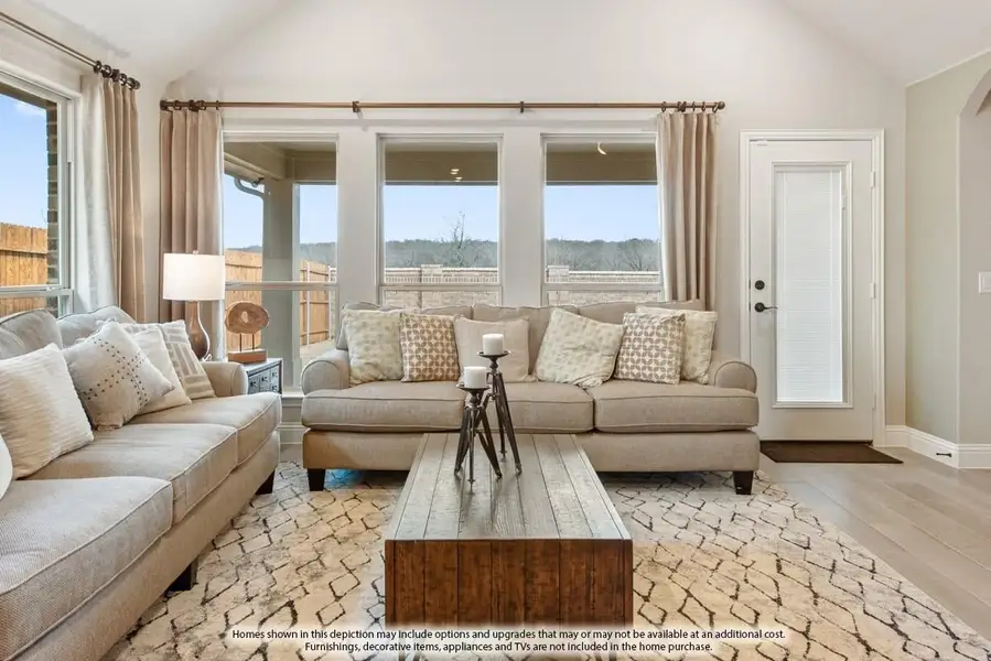 Living room with vaulted ceiling, two beige sofas, wood coffee table, and large windows with natural light.