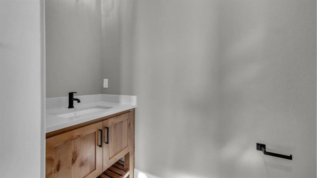 Bathroom vanity featuring a wood-finish cabinet, white countertop, integrated sink, and matte black faucet Bathroom vanity featuring a wood-finish cabinet, white countertop, integrated sink, and matte black faucet