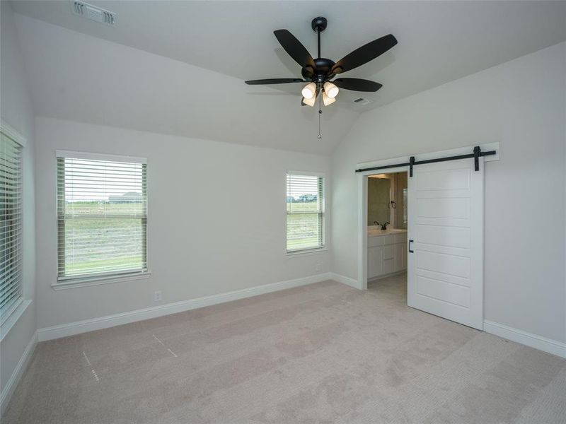 Unfurnished bedroom featuring a barn door, lofted ceiling, light colored carpet, ensuite bathroom, and ceiling fan Unfurnished bedroom featuring a barn door, lofted ceiling, light colored carpet, ensuite bathroom, and ceiling fan