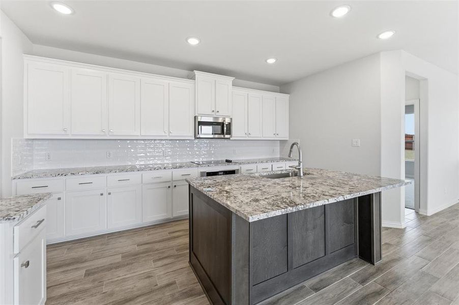 Kitchen featuring wood tiled floors, dual tone cabinetry, stainless steel microwave, light stone counters, and decorative backsplash