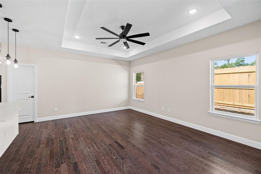 Spacious room featuring dark wood-finish flooring, a tray ceiling with recessed lighting and a black ceiling fan, and light-toned walls