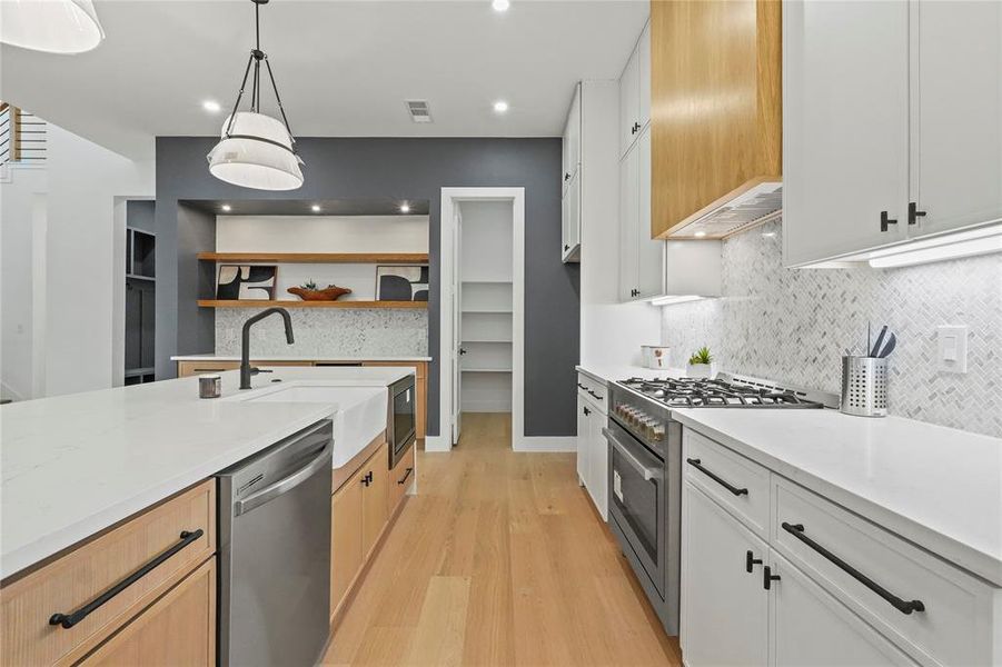 Kitchen featuring stainless steel appliances, light stone countertops, light wood-style floors, hanging light fixtures, and two tone cabinets