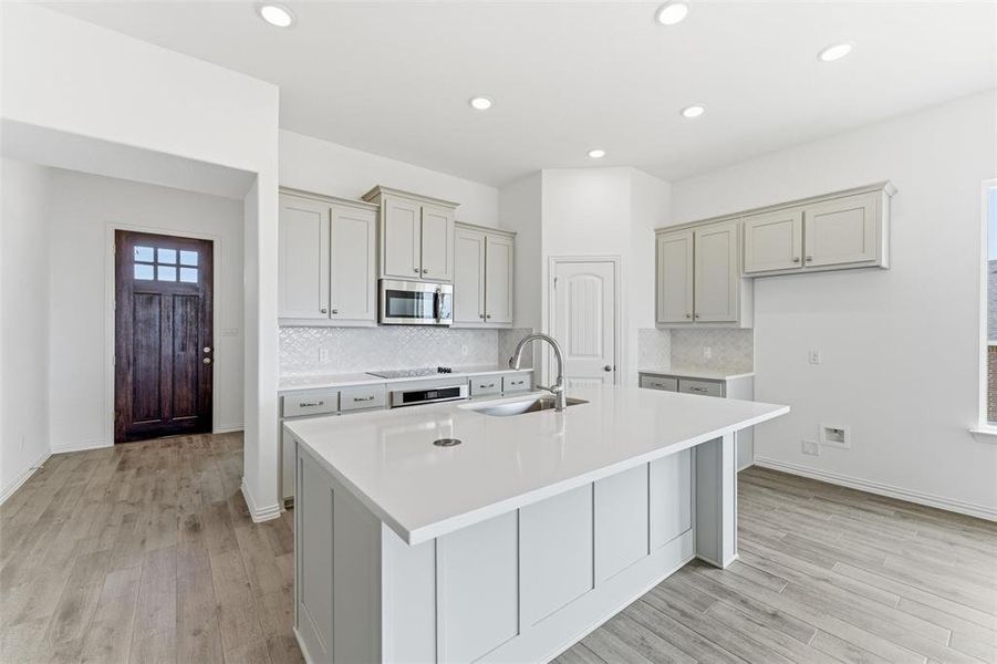 Kitchen with a kitchen island with sink, light wood finished floors, stainless steel microwave, oven, and recessed lighting