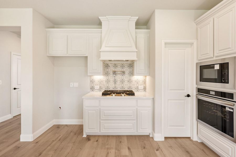 White kitchen with decorative range hood, patterned tile backsplash, gas cooktop, and built-in stainless steel oven and microwave
