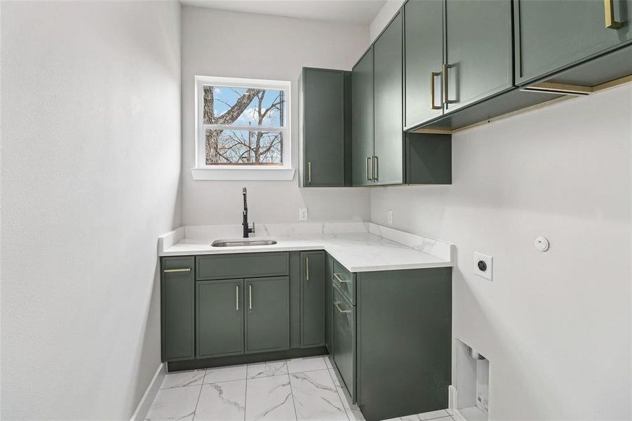 Laundry room featuring dark green cabinetry with brass hardware, a white countertop, and a stainless steel sink with a matte black faucet