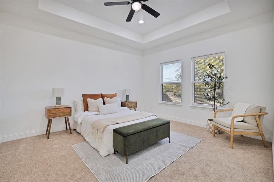 Bedroom featuring ceiling fan, light colored carpet, and a tray ceiling