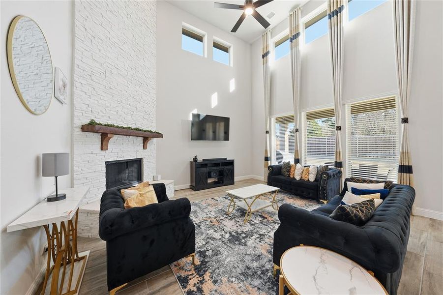 Living room featuring a fireplace, a ceiling fan, light wood-style floors, and a towering ceiling