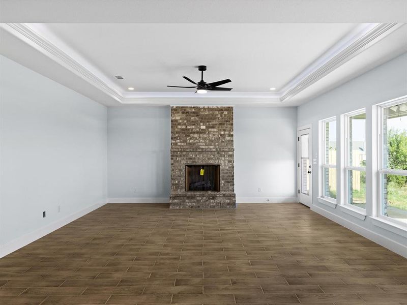 Unfurnished living room featuring dark wood-style floors, a ceiling fan, a tray ceiling, a fireplace, and recessed lighting