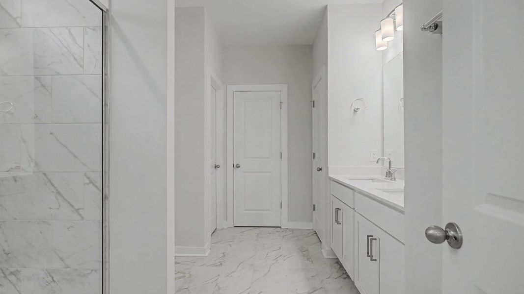 Beautiful and clean white bathroom with quartz countertops and marble-style tile flooring and shower walls