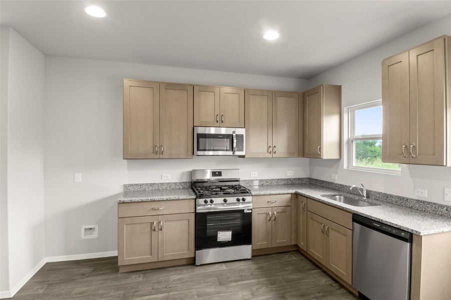 Kitchen featuring appliances with stainless steel finishes, wood finished floors, light brown cabinetry, and recessed lighting
