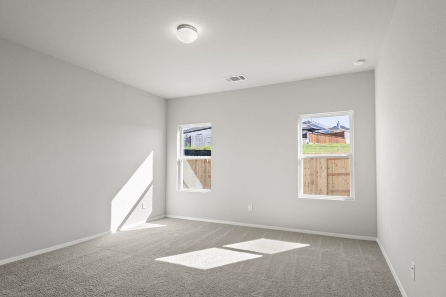 Image of a primary bedroom with tan carpeting and light grey painted walls with two windows
