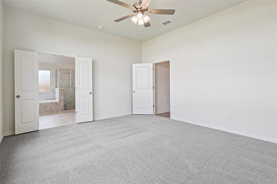 Unfurnished bedroom featuring light carpet, ensuite bathroom, and ceiling fan