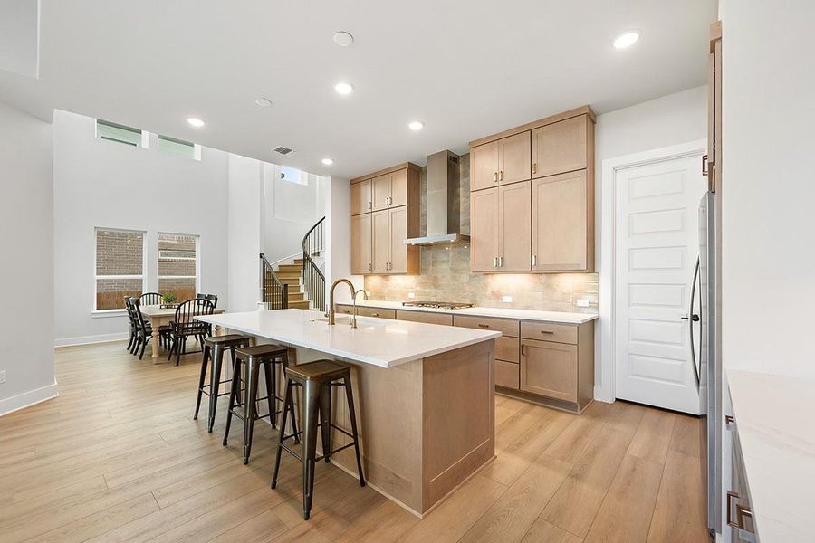 An open kitchen showcases warm wood cabinetry, stone countertops, and light-toned hardwood flooring.
