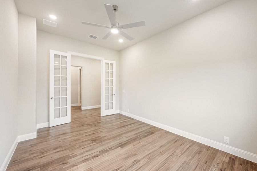 Empty room with hardwood floors, ceiling fan, and white French doors leading to hallway