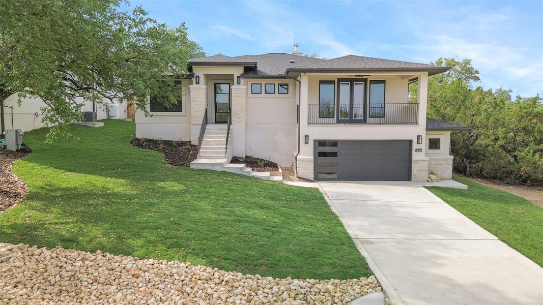 Prairie-style home featuring a front lawn, stucco siding, concrete driveway, and a balcony Prairie-style home featuring a front lawn, stucco siding, concrete driveway, and a balcony