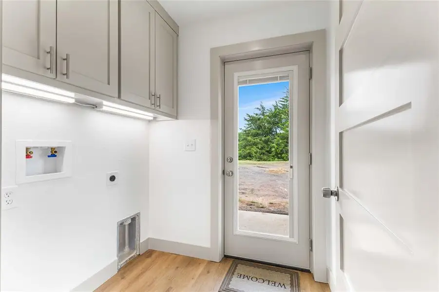 Washroom featuring cabinet space, hookup for an electric dryer, light wood finished floors, baseboards, and hookup for a washing machine Washroom featuring cabinet space, hookup for an electric dryer, light wood finished floors, baseboards, and hookup for a washing machine