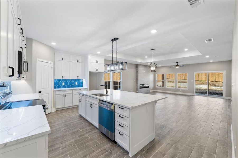 Kitchen with white cabinetry, light stone counters, appliances with stainless steel finishes, pendant lighting, and a kitchen island with sink