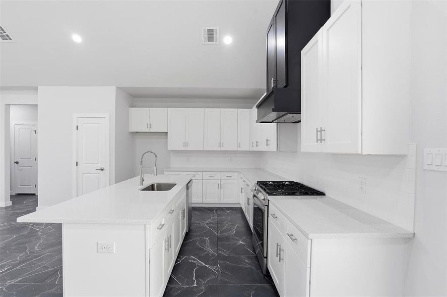 Modern kitchen featuring white cabinetry, quartz countertops, a large island with an undermount sink, a stainless steel gas range, and dark-toned marble-look flooring