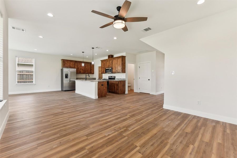 Unfurnished living room with light wood look floors, visible vents, a sink, baseboards, and ceiling fan Unfurnished living room with light wood look floors, visible vents, a sink, baseboards, and ceiling fan