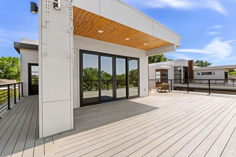 The full scale of the rooftop deck becomes clear from this angle — an expansive, open decked platform with the covered section anchoring one end and the cable railing enclosing the full perimeter at an elevation that puts the neighborhood canopy eye-level.