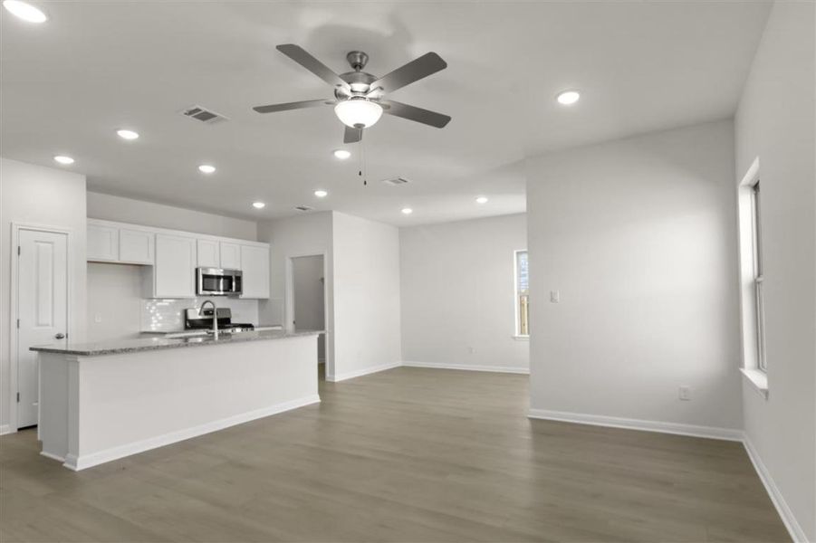 Kitchen featuring wood finished floors, a sink, white cabinetry, decorative backsplash, and stainless steel microwave