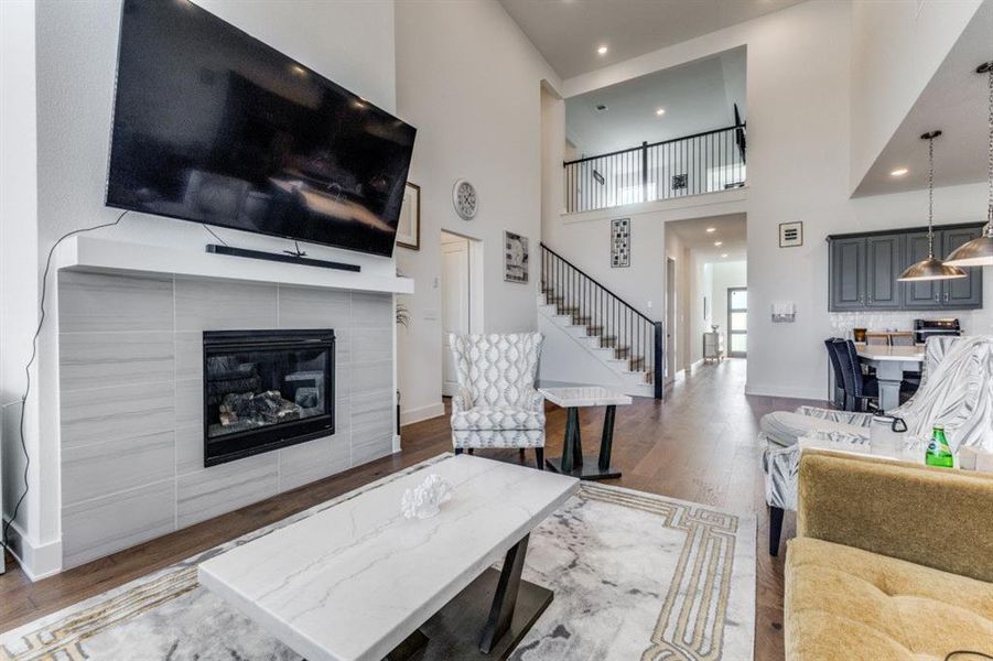 Living area with a tiled fireplace, wood finished floors, recessed lighting, and a high ceiling