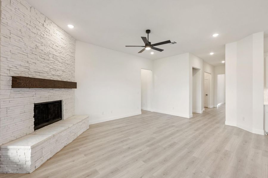 Open living room with white stacked stone fireplace, wood mantel, light hardwood floors, and ceiling fan Open living room with white stacked stone fireplace, wood mantel, light hardwood floors, and ceiling fan