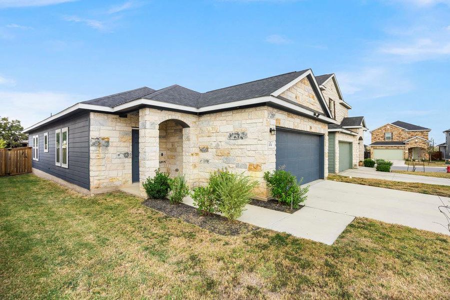 View of front of house featuring stone siding, a front yard, and concrete driveway