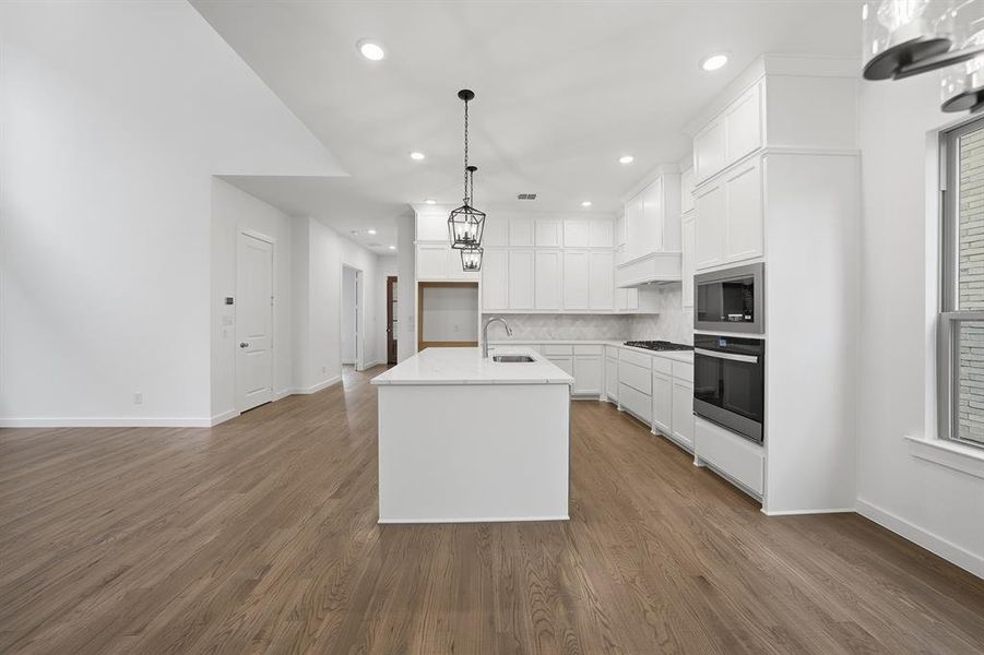 Kitchen featuring white cabinets, decorative light fixtures, an island with sink, appliances with stainless steel finishes, and dark wood-type flooring