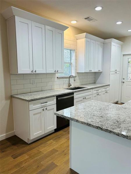 Kitchen with white cabinetry, a wealth of natural light, stainless steel dishwasher, and light hardwood / wood-style floors