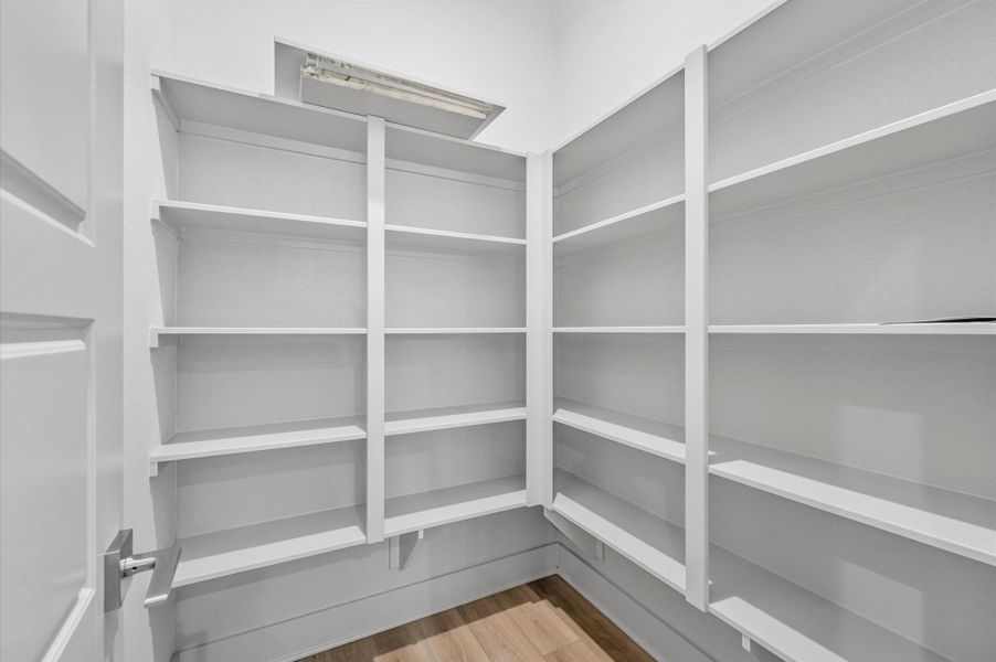 This photo shows a bright, well-organized pantry with ample white shelving for storage, situated on a hardwood floor. This photo shows a bright, well-organized pantry with ample white shelving for storage, situated on a hardwood floor.