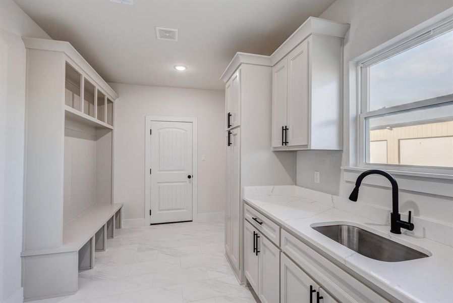 Kitchen with white cabinets, plenty of natural light, light stone counters, and sink