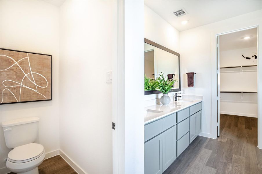 This photo showcases a modern bathroom with a spacious vanity and dual sinks, complemented by a large mirror. The room is bright, featuring sleek cabinetry and wood flooring, with access to a walk-in closet. A separate toilet area adds privacy, adorned with contemporary artwork. This photo showcases a modern bathroom with a spacious vanity and dual sinks, complemented by a large mirror. The room is bright, featuring sleek cabinetry and wood flooring, with access to a walk-in closet. A separate toilet area adds privacy, adorned with contemporary artwork.