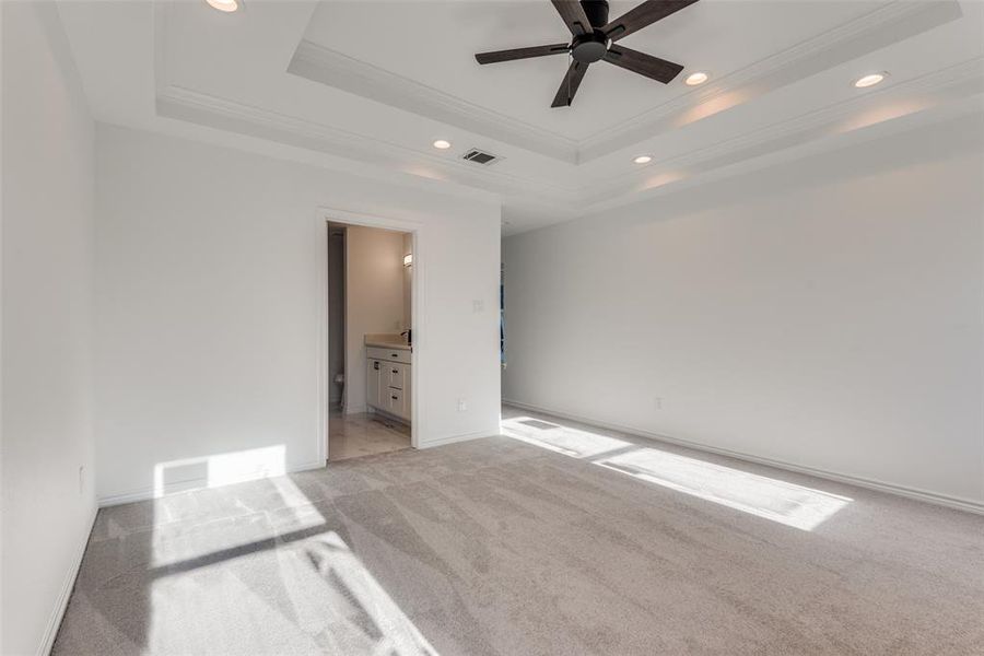 Unfurnished bedroom with a tray ceiling, ceiling fan, ornamental molding, and ensuite bathroom