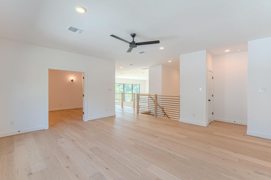 This photo showcases a bright, open-concept living space with light wood flooring, a ceiling fan, and recessed lighting. It features a railing with a modern design and a separate room, ideal for an office or additional living area. The space is airy with ample natural light.