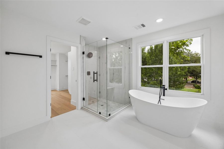 Centered around a freestanding soaking tub positioned beside oversized windows, the primary bath was designed to maximize natural light and surrounding greenery views. A spacious walk-in shower, modern plumbing fixtures, and clean architectural finishes complete the spa-inspired layout.