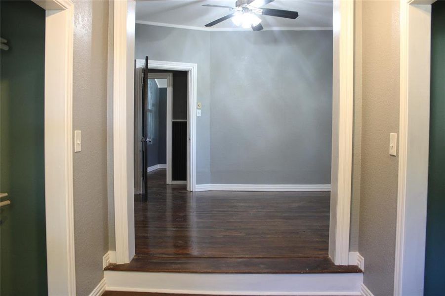 Corridor featuring ornamental molding, dark wood-type flooring, and a textured wall Corridor featuring ornamental molding, dark wood-type flooring, and a textured wall