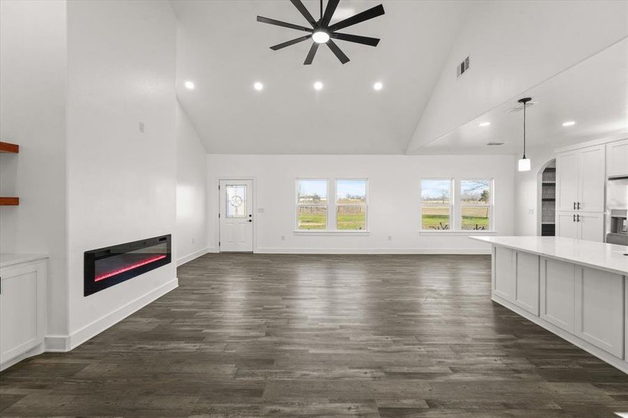 Unfurnished living room featuring dark wood-type flooring, high vaulted ceiling, and ceiling fan