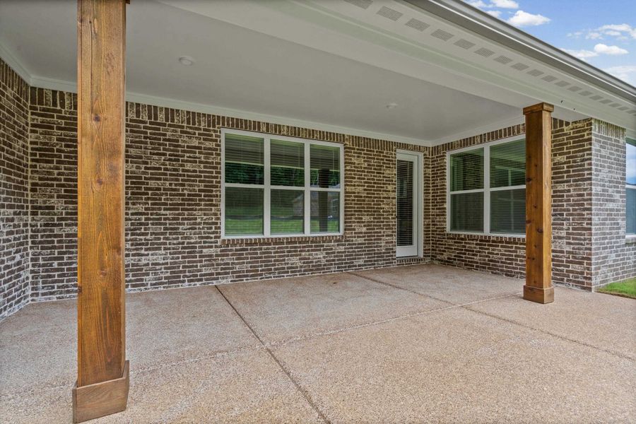 Covered patio with an exposed aggregate concrete surface, brick exterior wall, and wood-wrapped support columns Covered patio with an exposed aggregate concrete surface, brick exterior wall, and wood-wrapped support columns