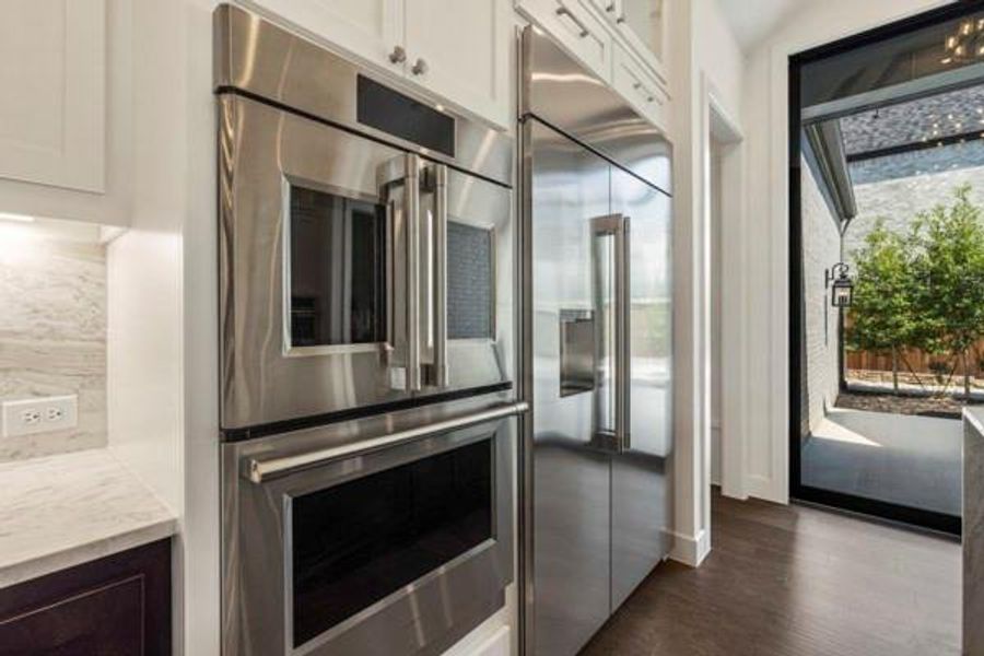 Kitchen featuring stainless steel appliances, glass insert cabinets, dark wood finished floors, light stone countertops, and white cabinets Kitchen featuring stainless steel appliances, glass insert cabinets, dark wood finished floors, light stone countertops, and white cabinets
