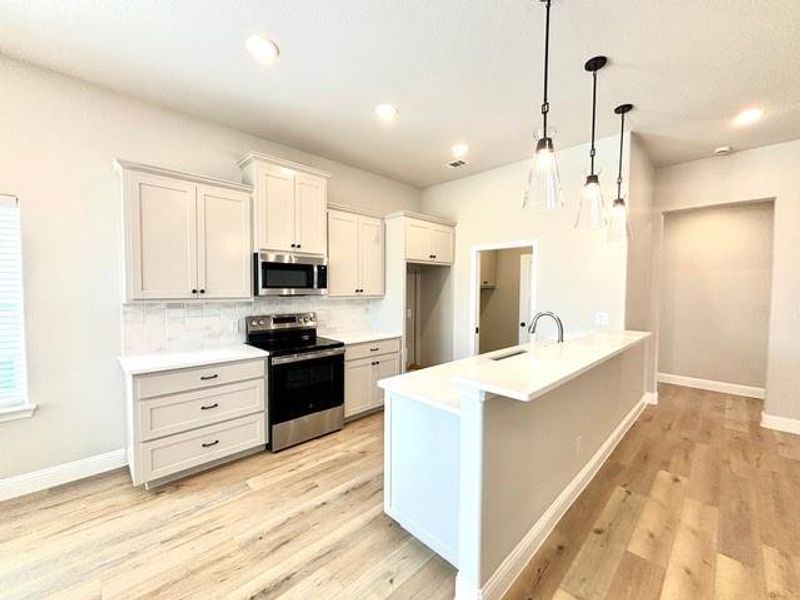 Kitchen featuring white cabinets, sink, decorative backsplash, decorative light fixtures, and stainless steel appliances