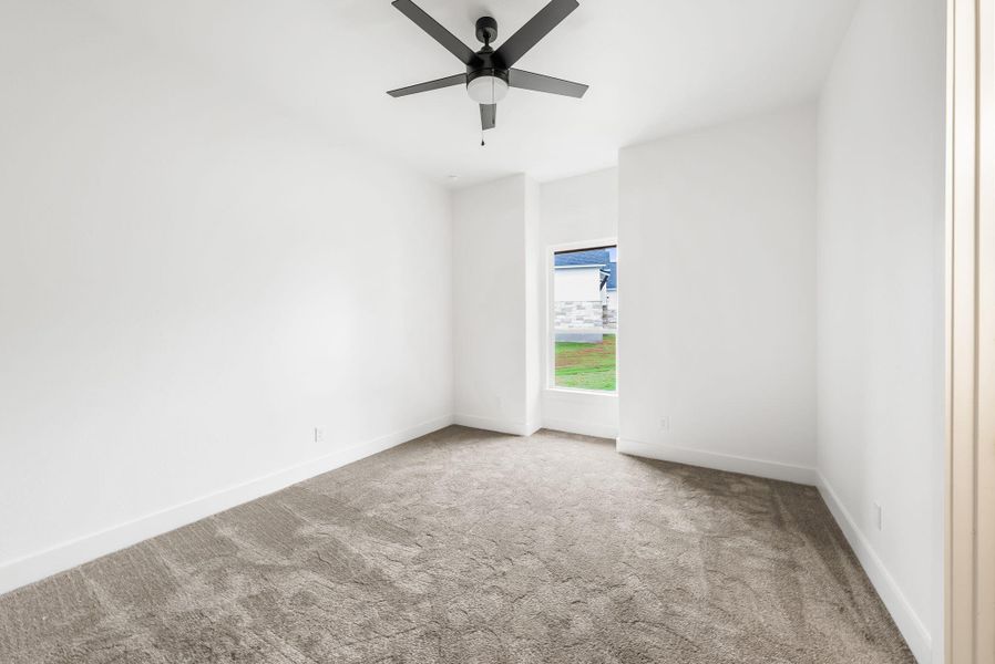 A well-lit bedroom features plush carpeting and a modern ceiling fan, offering a comfortable personal retreat.