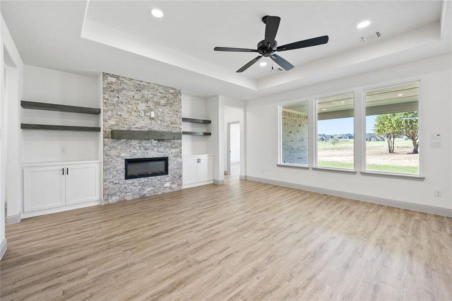 Unfurnished living room with a raised ceiling, light wood-style floors, a stone fireplace, ceiling fan, and recessed lighting