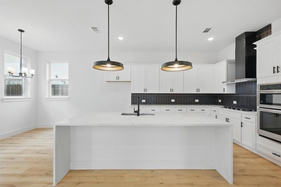 Kitchen with a sink, wall chimney range hood, stainless steel appliances, a chandelier, and tasteful backsplash