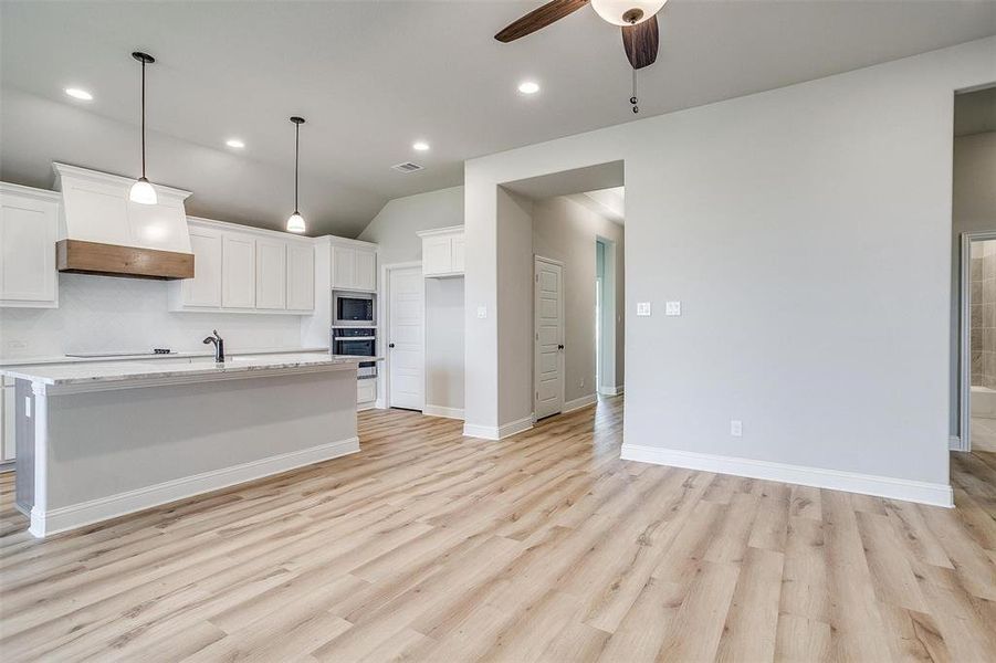 Kitchen with appliances with stainless steel finishes, light wood-type flooring, premium range hood, and white cabinetry