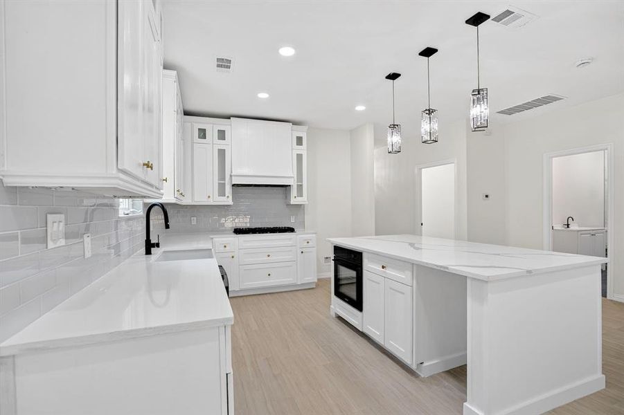 Kitchen featuring an expansive white stone countertop island with an integrated oven and three pendant lights