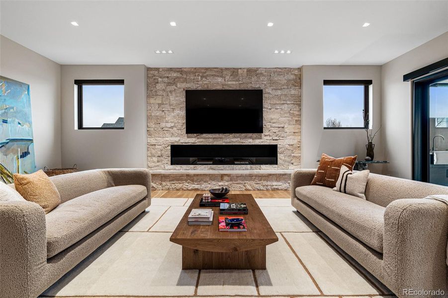 Cinematic bliss in the cozy family room, where every scene comes to life with 5.1 surround sound, an 85" Samsung 4K TV, in ceiling speakers & in wall subwoofer. EcoSmart Flex Series fireplace with textured stone and Pental Quartz slab bench top.