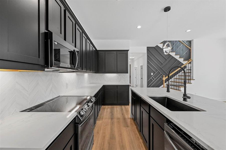 Kitchen with stainless steel appliances, decorative light fixtures, decorative backsplash, sink, and light wood-type flooring