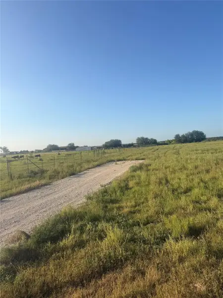 A gravel driveway winds through open pastures under a clear blue sky.