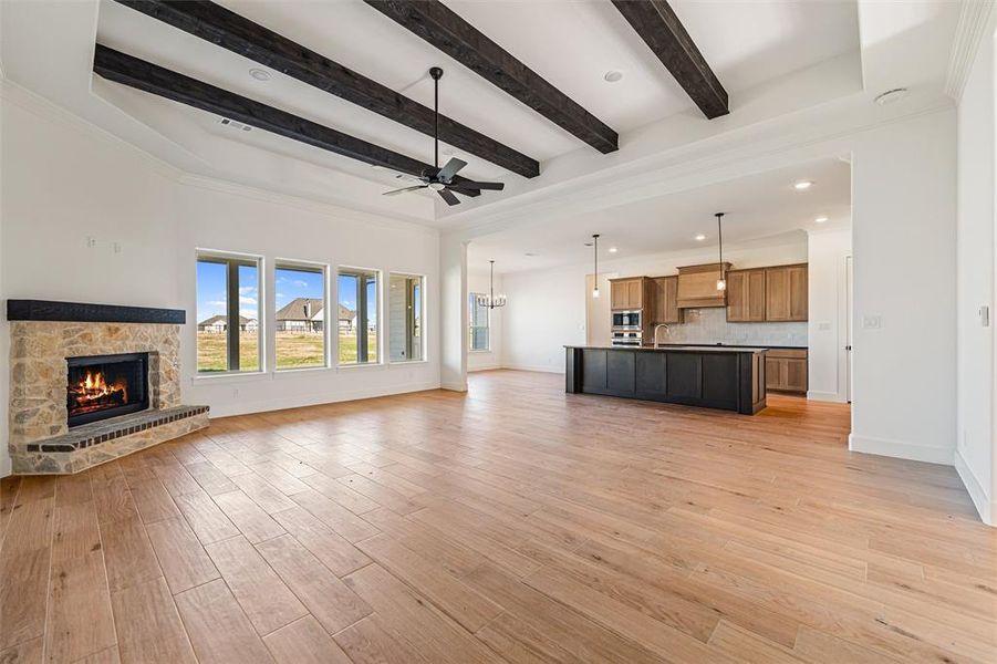 Unfurnished living room featuring light wood finished floors, a stone fireplace, a ceiling fan, recessed lighting, and a chandelier